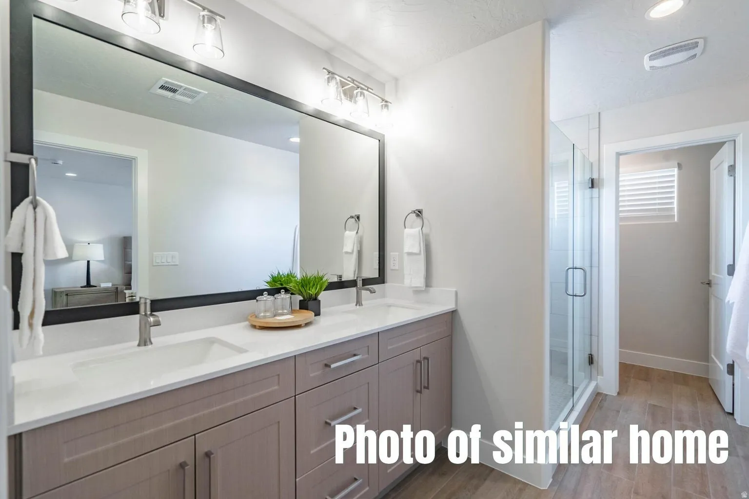 Dual vanity with integrated sinks, brushed nickel fixtures, quartz-finish countertop, full-width framed mirror, and a glass-enclosed shower