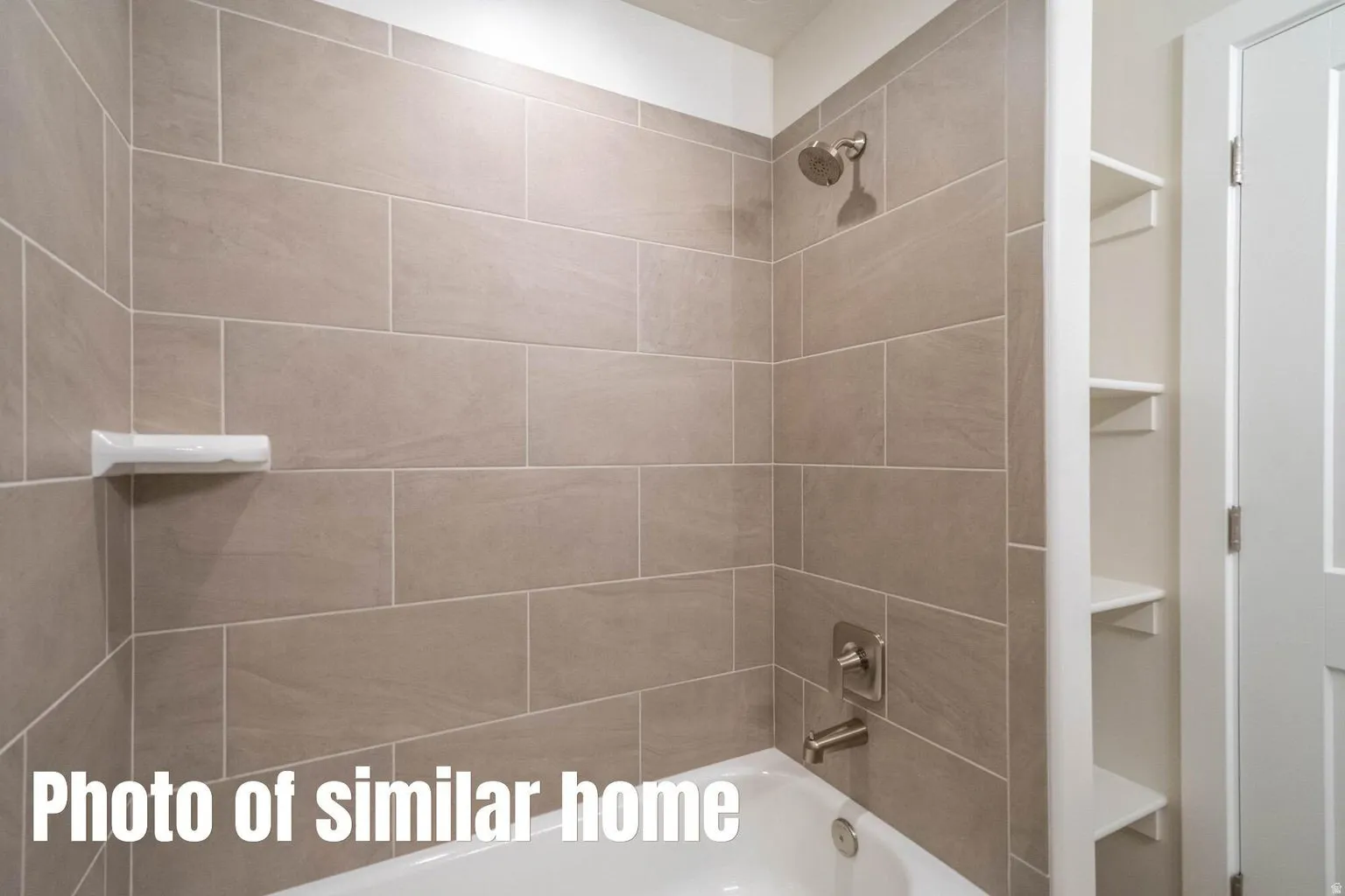 Shower/tub combination with tile surround, brushed nickel fixtures, and built-in shelving