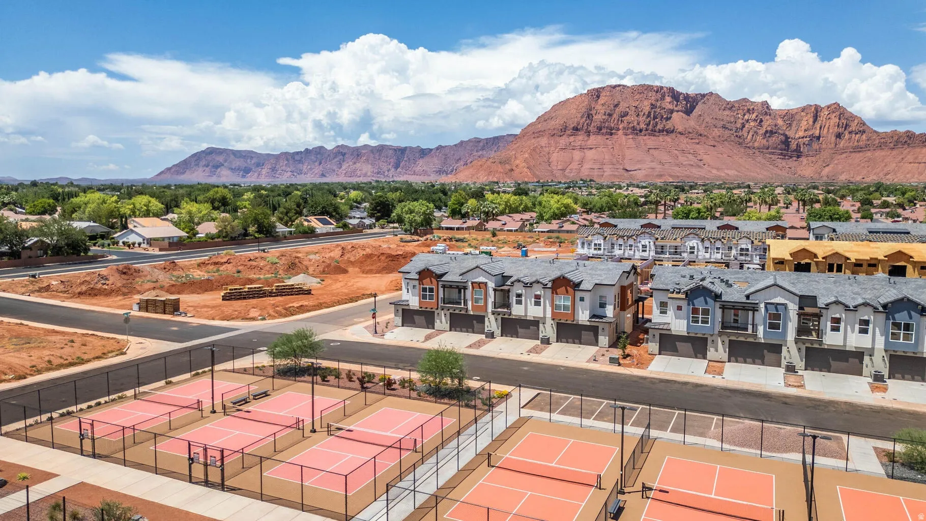 Multiple hard-surface courts, residential structures featuring varied facades, and a mountainous backdrop