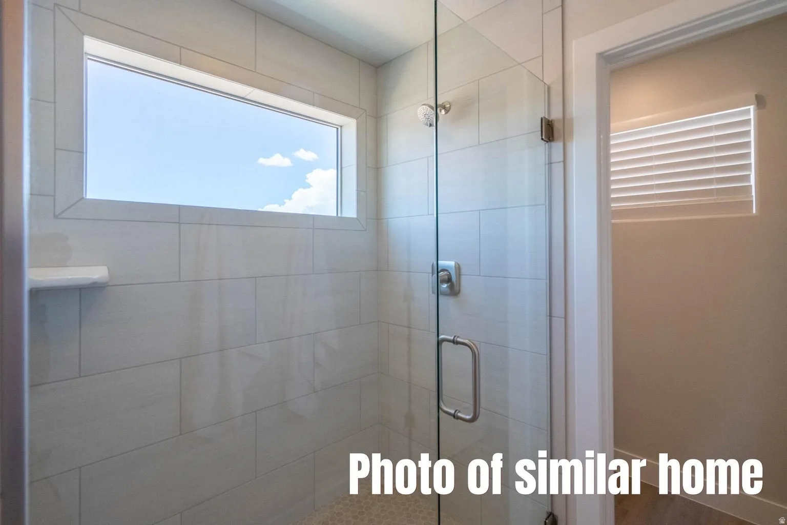 Walk-in shower with clear glass enclosure, tiled walls, and fixed window