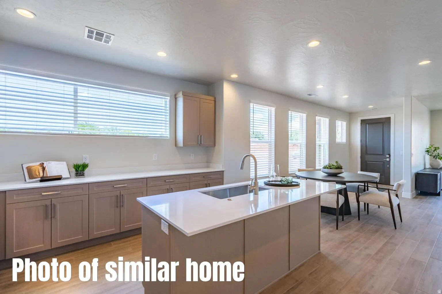 Open concept design with recessed lighting, large kitchen island with integrated sink, light-toned wood-finish flooring, and shaker-style cabinetry with chrome hardware