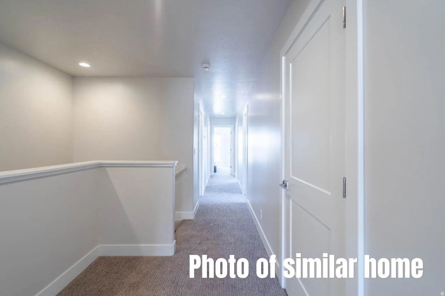 Recessed lighting and a neutral color palette enhance this interior space featuring a hallway with panel doors and carpeted flooring