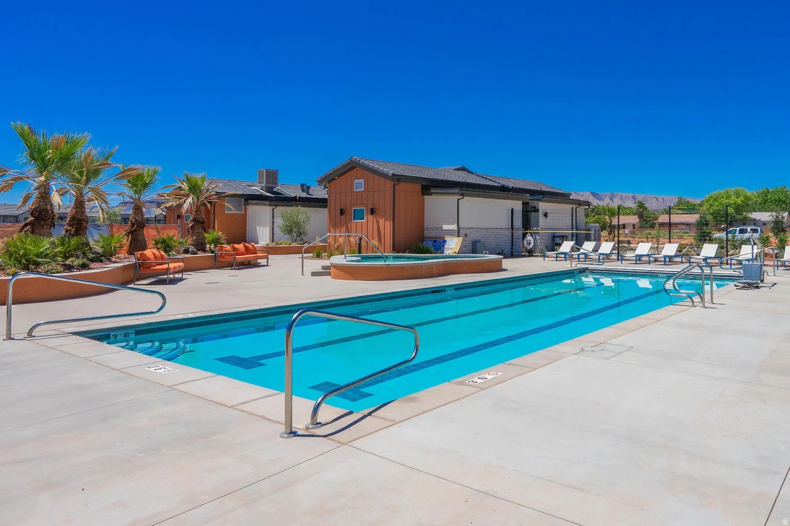 Outdoor swimming pool with integrated spa, surrounded by a concrete deck with lounge seating, and mature palm trees