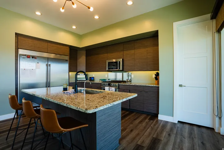 Kitchen featuring wood-finish flooring, an island with a stone countertop, built-in stainless steel appliances, dark wood-finish cabinetry, and recessed lighting