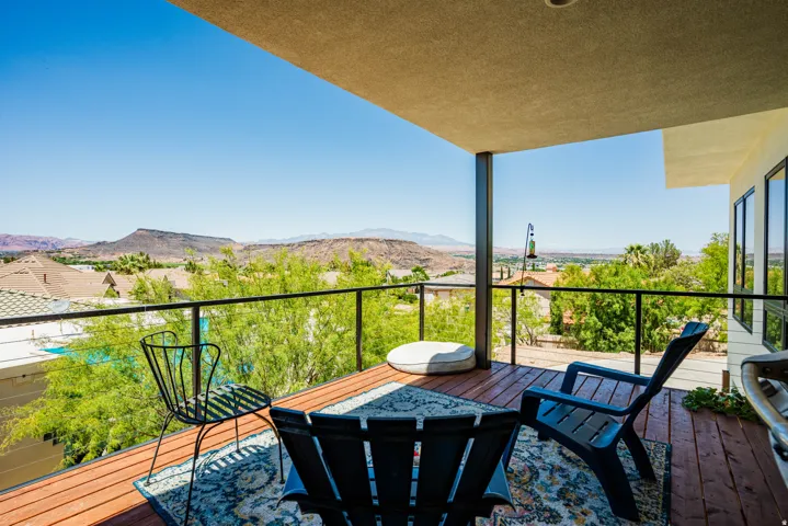 Covered outdoor deck with wood-finish flooring, glass railing, and distant mountain scenery