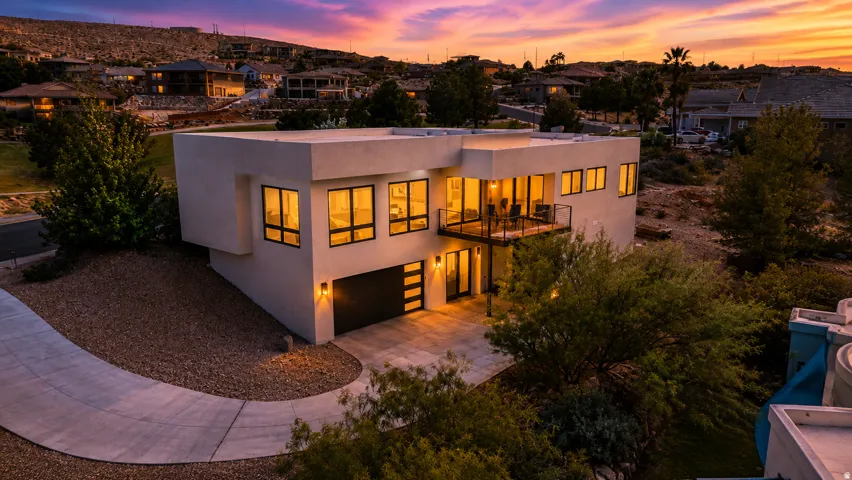 Contemporary architecture with multiple large windows, an upper-level balcony, a lower-level patio, and a two-car garage