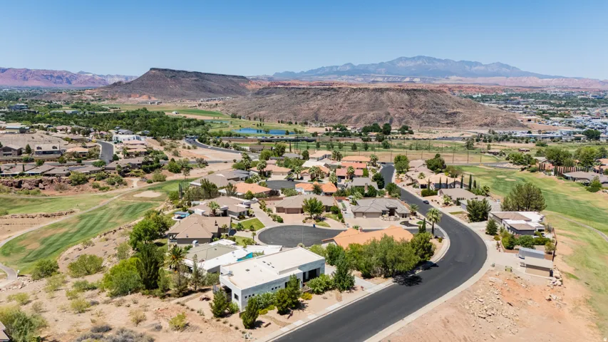 Residential area with a curved street, surrounding golf course, and distant mountains