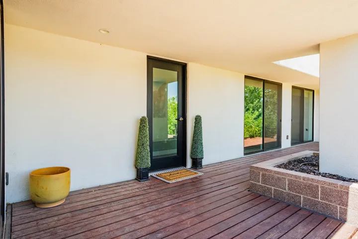 Covered outdoor patio featuring wood-finish decking, a built-in planter with stone-block detailing, and sliding glass doors