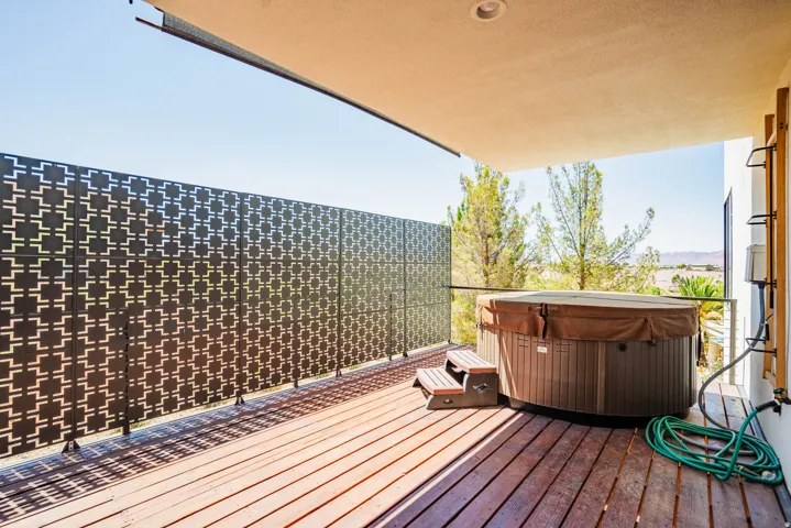 Private outdoor deck featuring a hot tub, wood decking, and a decorative metal privacy screen