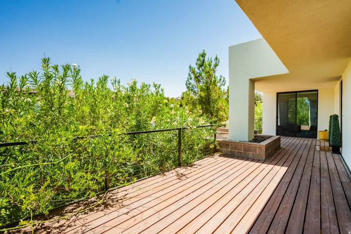 Expansive wood-finish deck with a metal railing, featuring a built-in planter and sliding glass door access