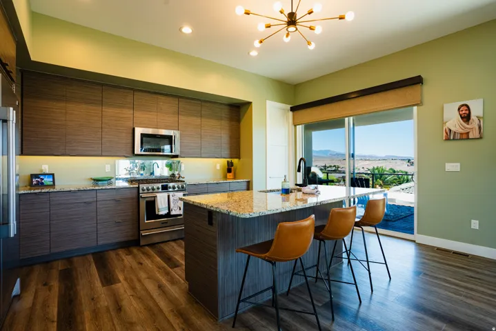 Gourmet kitchen with stainless steel appliances, wood-finish flooring, full-height cabinetry, a large center island, and expansive glass sliding doors