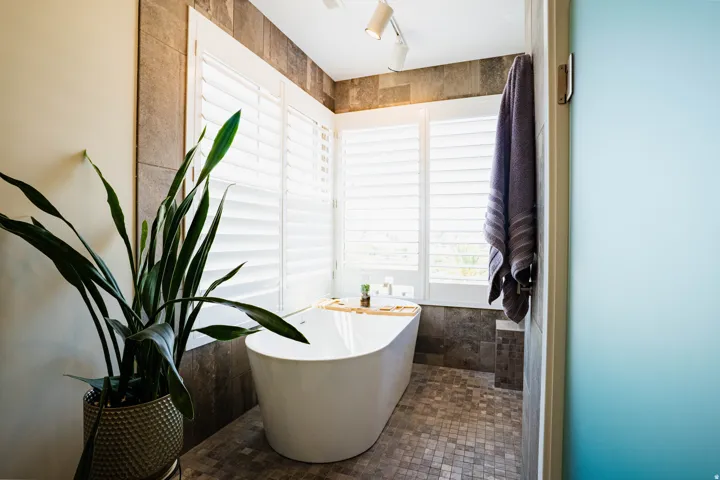 Freestanding soaking tub with a tiled surround, plantation shutters, track lighting, and mosaic tile flooring