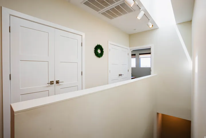 Modern hallway featuring dual white six-panel closet doors with brushed brass hardware, a clean white shaker-style door with matching hardware, recessed and track lighting throughout, and neutral wall finishes with crisp white trim detailing