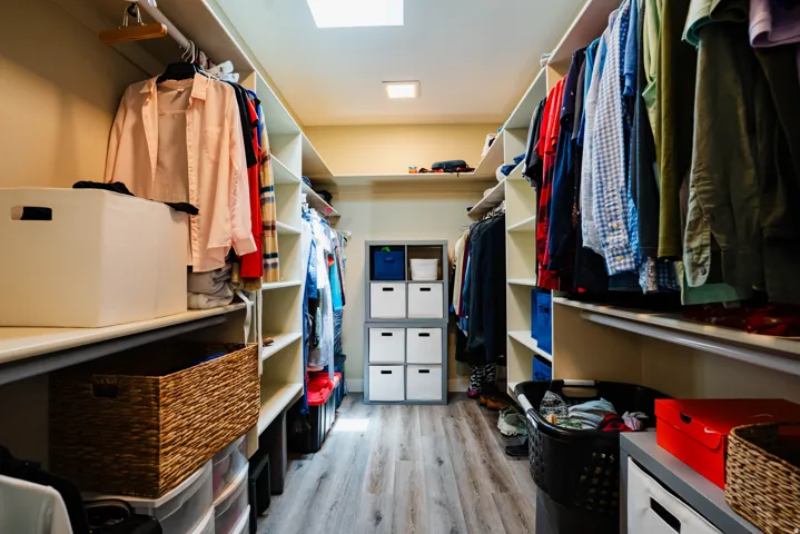 Custom closet organization system with ample shelving, hanging rods, central storage units, and wood-finish flooring