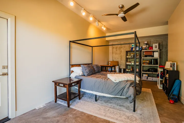 Track lighting, ceiling fan, and concrete accent wall