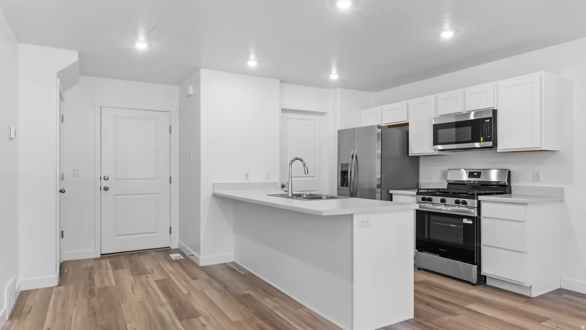Kitchen with wood-finish flooring, white cabinetry, stainless steel appliances, and an island with a sink and countertop
