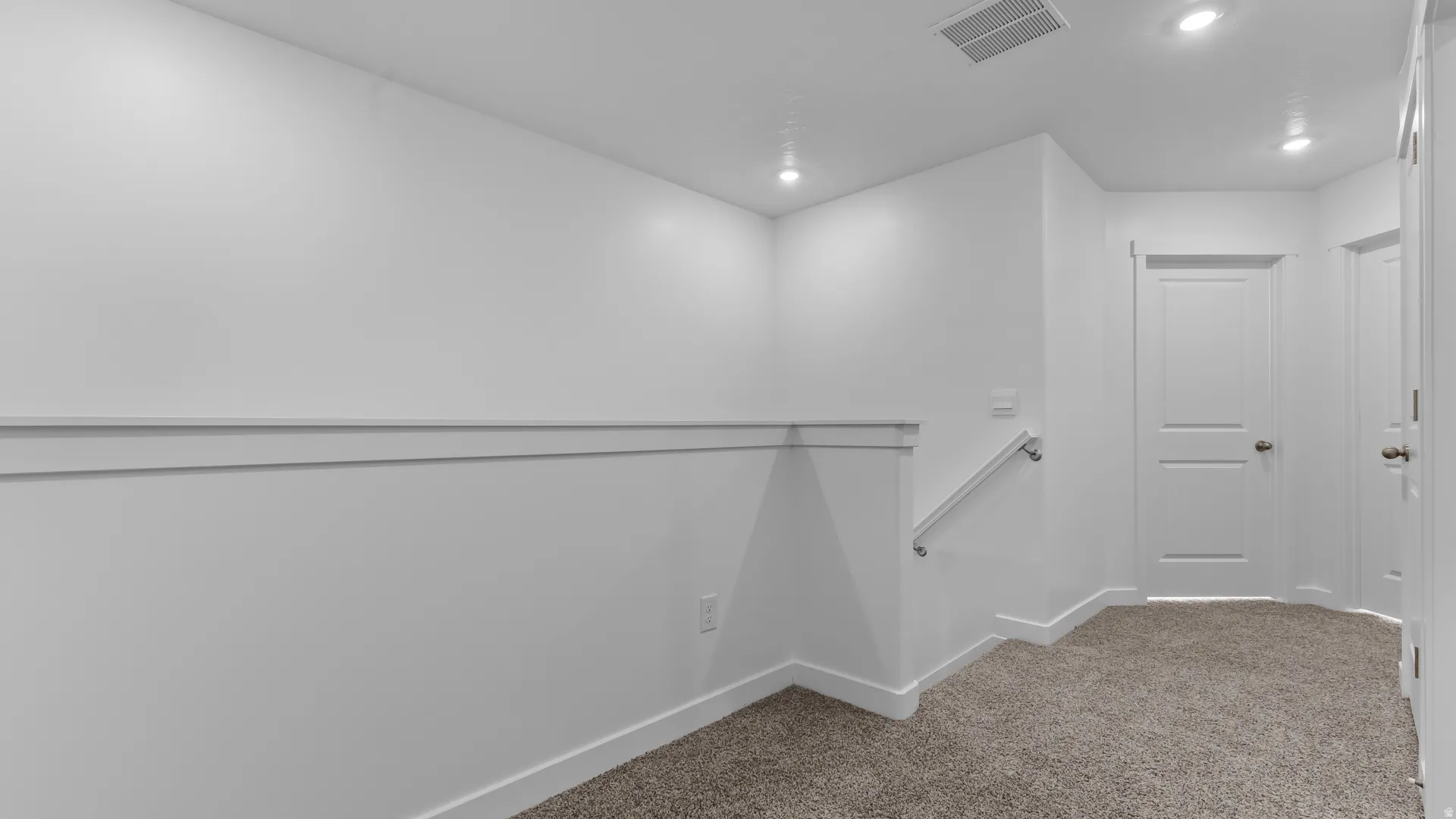Recessed lighting illuminates the neutral carpet and white walls with decorative chair rail molding