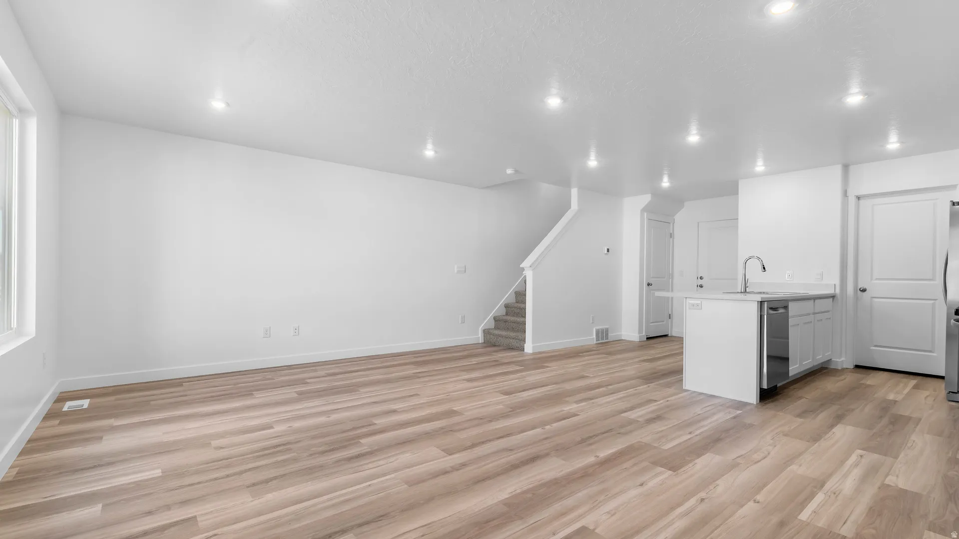 Open-concept living area featuring wood-finish flooring, recessed lighting, and a modern kitchen island with an integrated sink and stainless steel dishwasher