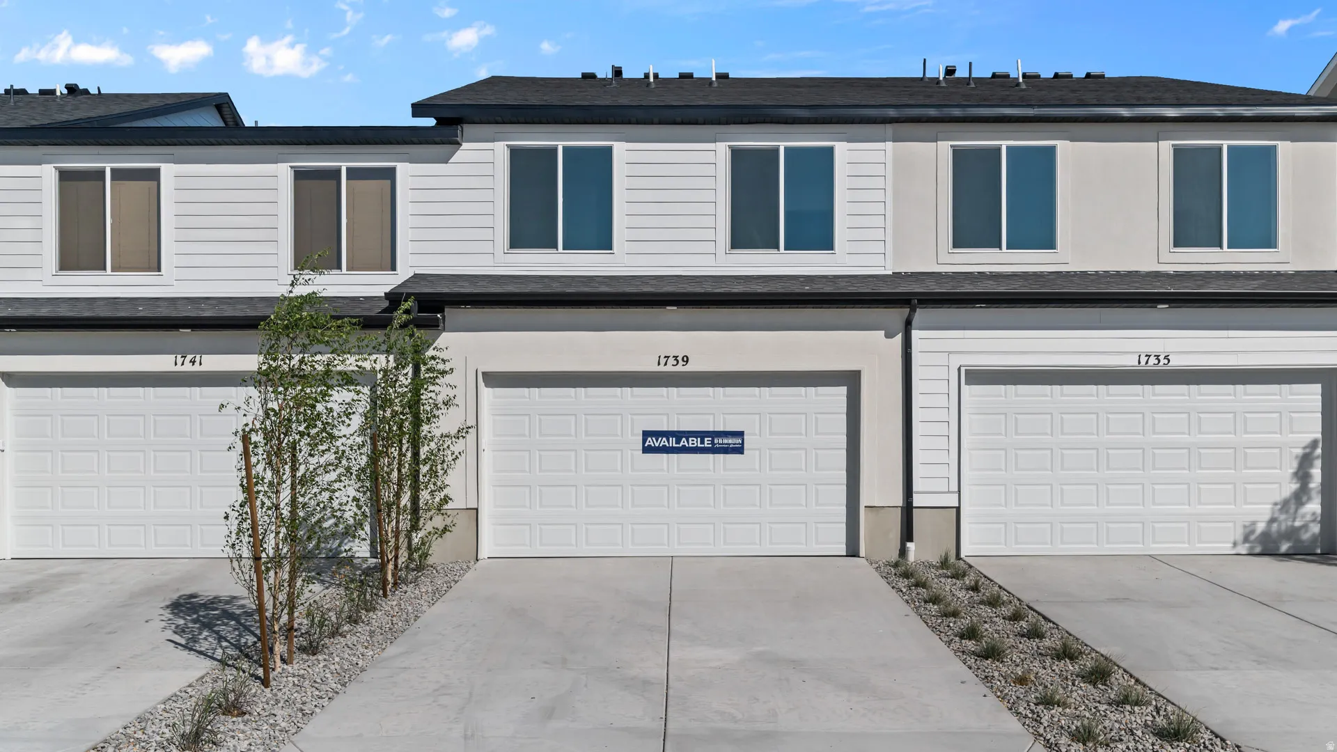 Modern townhome exterior featuring white horizontal siding, light stucco accents, a dark asphalt shingle roof, and white paneled garage doors