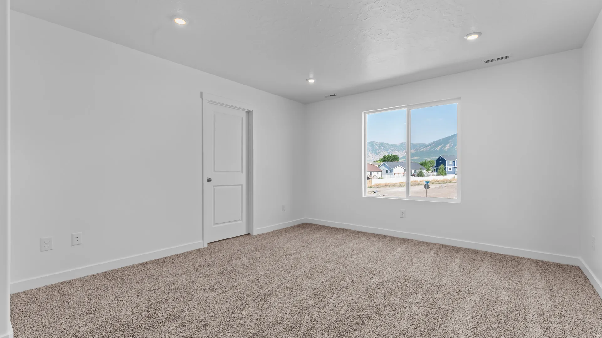 Recessed lighting, neutral-toned carpet, white walls, white two-panel door, and a window with a mountain backdrop