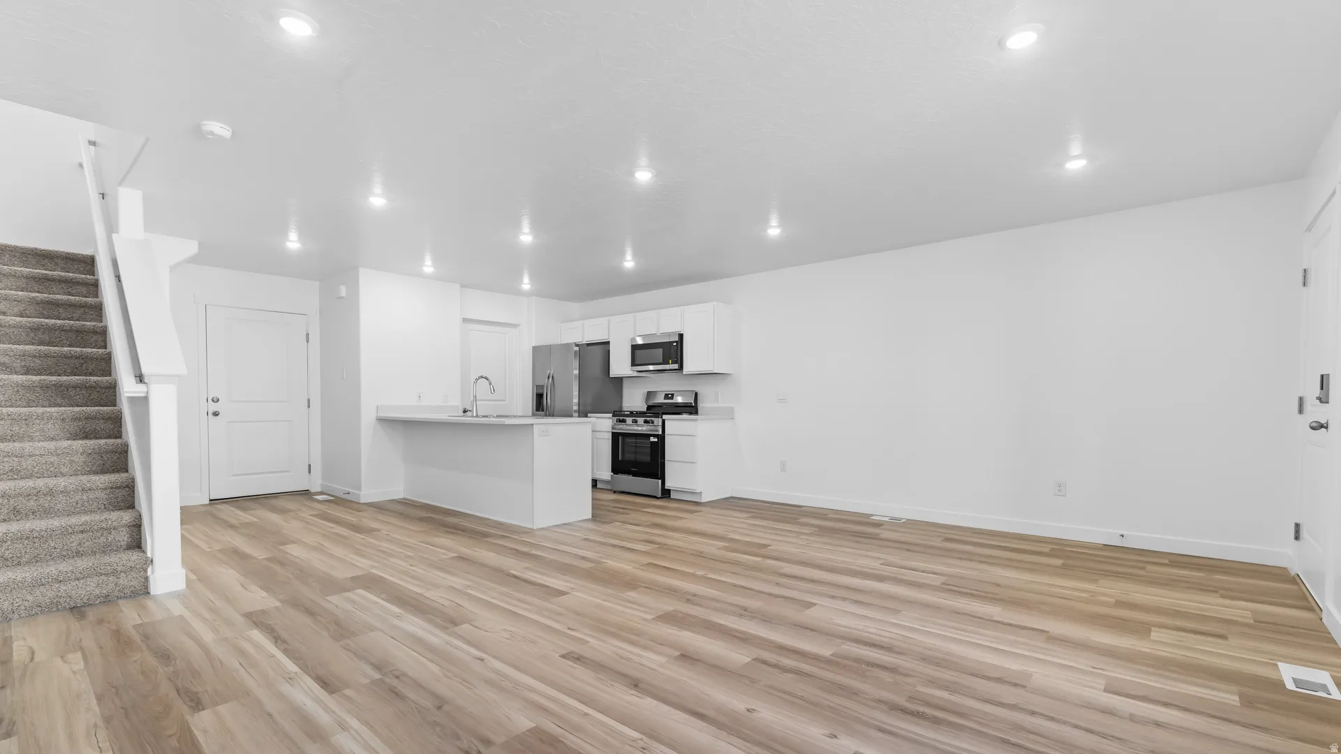 Open-concept living space with wood-finish flooring, white walls, and recessed lighting