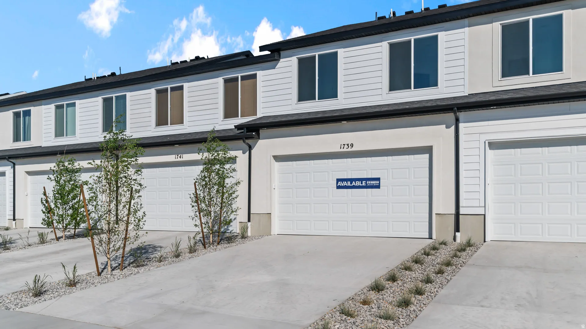Modern townhome exterior with horizontal siding, large windows, attached garage, concrete driveway, and landscaped rock beds