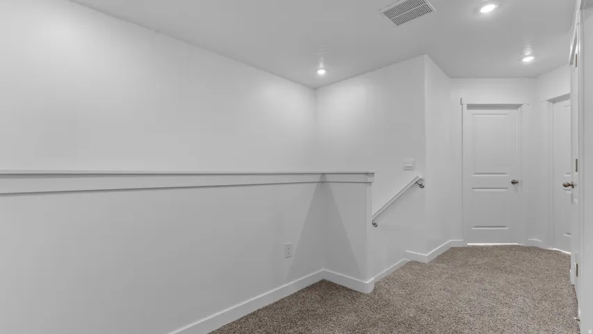 Recessed lighting illuminates the neutral carpet and white walls with decorative chair rail molding