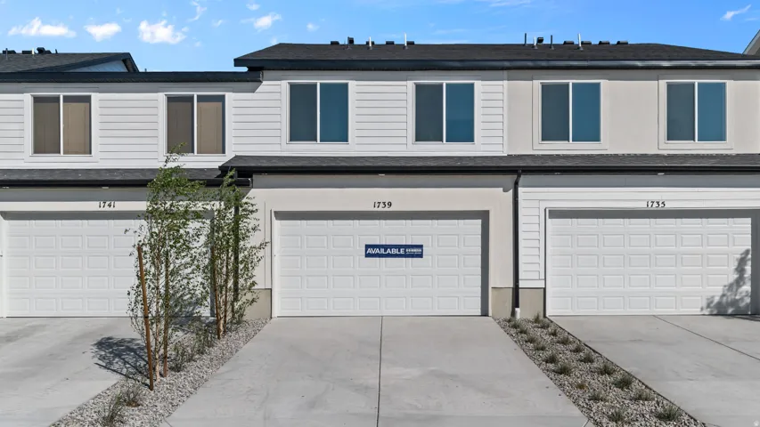 Modern townhome exterior featuring white horizontal siding, light stucco accents, a dark asphalt shingle roof, and white paneled garage doors