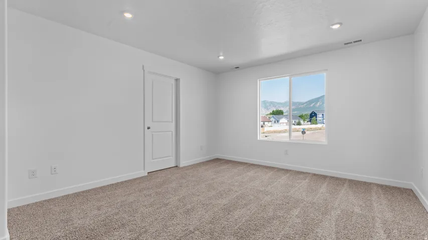 Recessed lighting, neutral-toned carpet, white walls, white two-panel door, and a window with a mountain backdrop