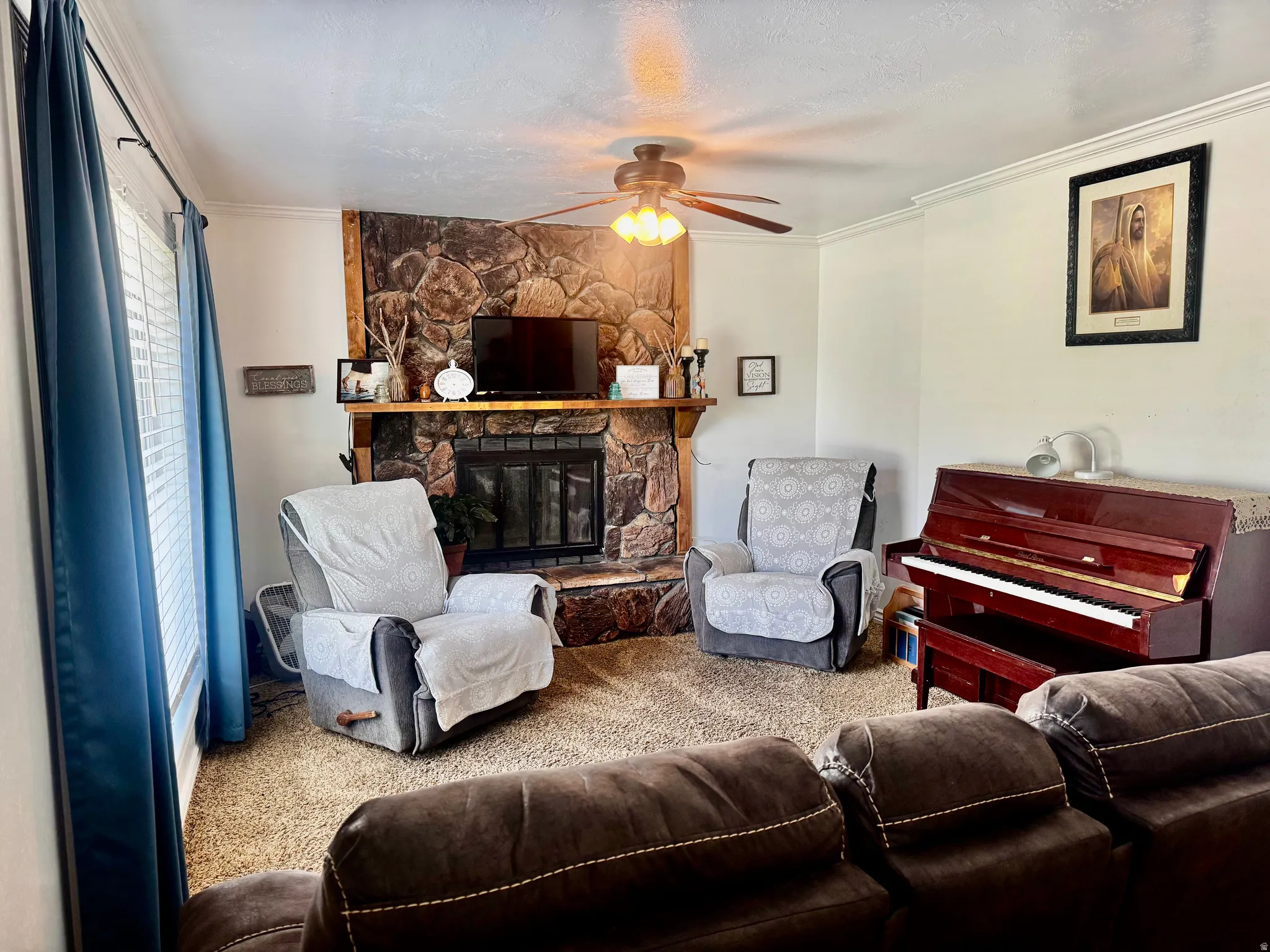 Stone-clad fireplace with wood mantel, ceiling fan with integrated lighting, and crown molding