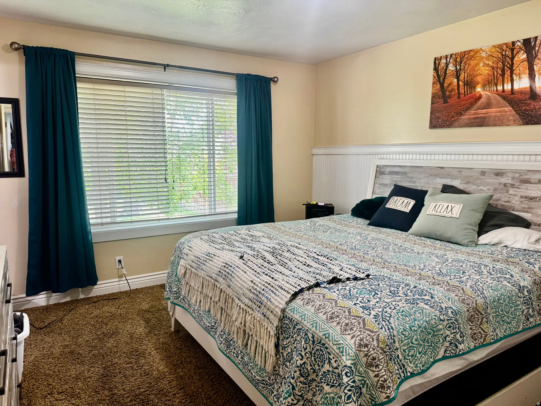 Carpeted bedroom featuring a large window with blinds, a headboard with wood paneling details, and a built-in wall paneling accent