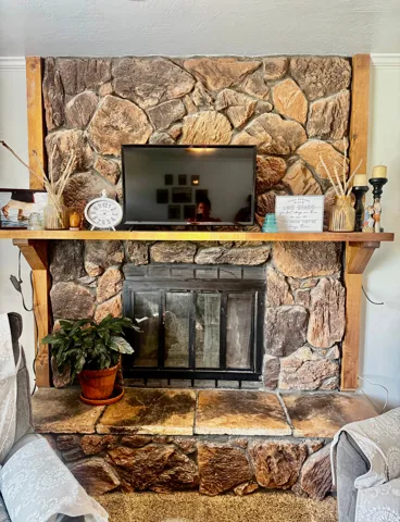 Stone-clad fireplace with a wood mantel and hearth, featuring an integrated firebox with glass doors