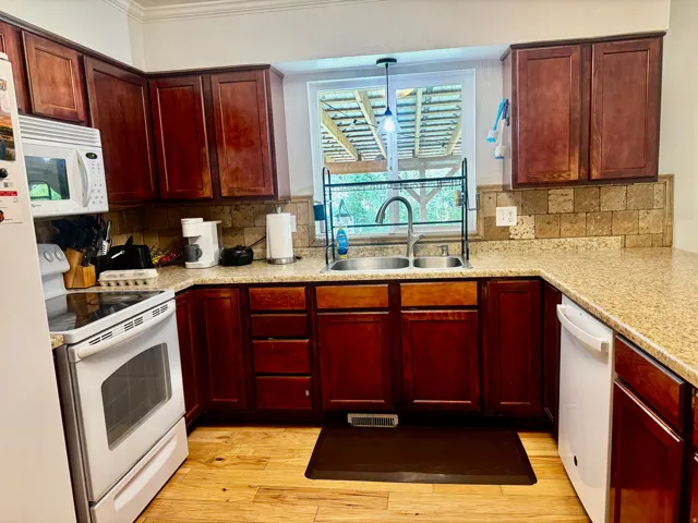 Wood-finish flooring, cherry-toned cabinetry, light-toned countertops, tile backsplash, and a double basin sink