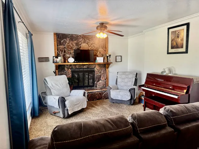 Stone-clad fireplace with wood mantel, ceiling fan with integrated lighting, and crown molding