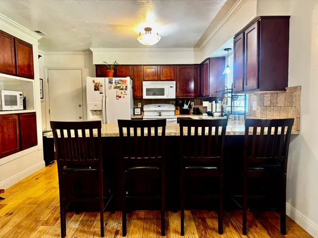 Kitchen featuring wood-finish flooring, dark wood cabinetry, a breakfast bar with a light-toned countertop, and white appliances