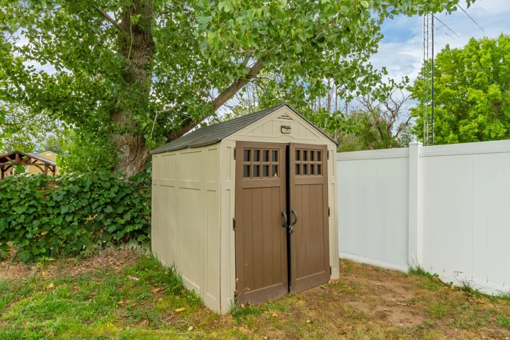 Storage shed with a gabled roof and double doors, situated beside a white privacy fence