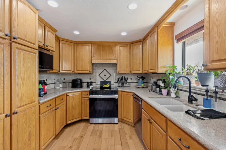 U-shaped kitchen featuring wood cabinetry, stone-finish countertops, tile backsplash, and wood-finish flooring