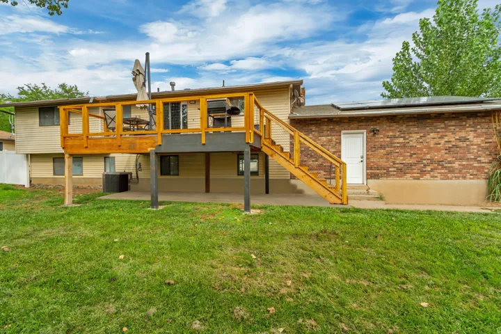 Multi-level exterior featuring a wood-deck balcony, brick facade, and ground-level patio