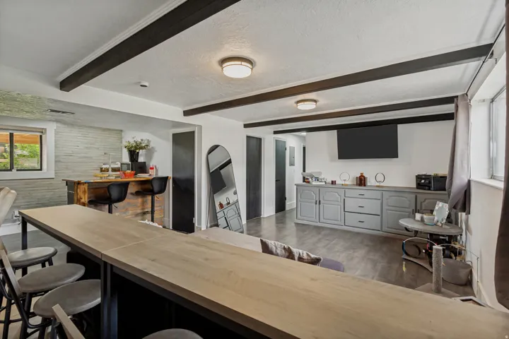 Exposed wood-finish beams, recessed lighting, LVP flooring, built-in cabinetry, and a stacked stone accent wall