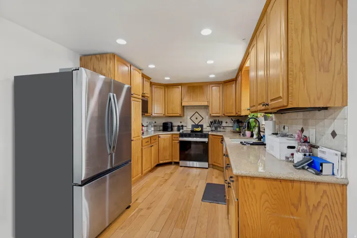 Kitchen featuring wood-finish cabinetry, stainless steel appliances, recessed lighting, and light-toned countertops with a tiled backsplash
