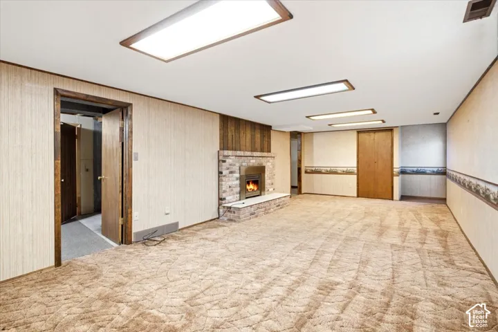 Spacious room featuring a brick fireplace with a visible firebox, ceiling-mounted rectangular light fixtures, and wall paneling