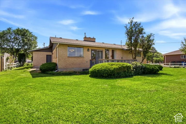 Expansive grass lawn featuring mature landscaping, a brick exterior, and a wood deck with sliding glass doors
