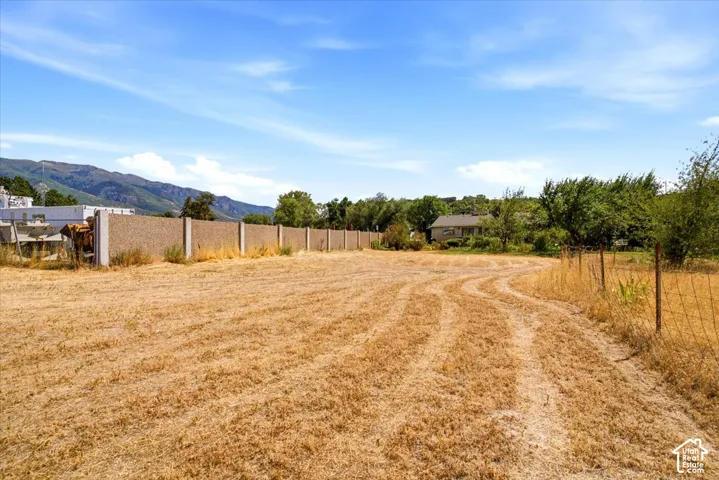 Expansive open field with natural ground cover, partial fencing, and distant mountain backdrop
