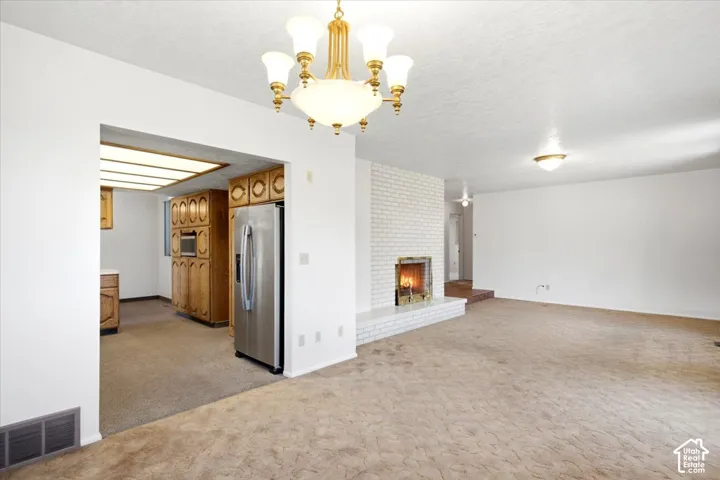 Spacious room with a white brick fireplace, recessed kitchen area with wood-finish cabinetry, and a stainless steel refrigerator