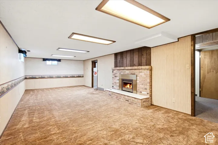 Brick fireplace with a metal insert, wood paneling, recessed fluorescent lighting, wall-to-wall carpeting, and wood-finish door frames