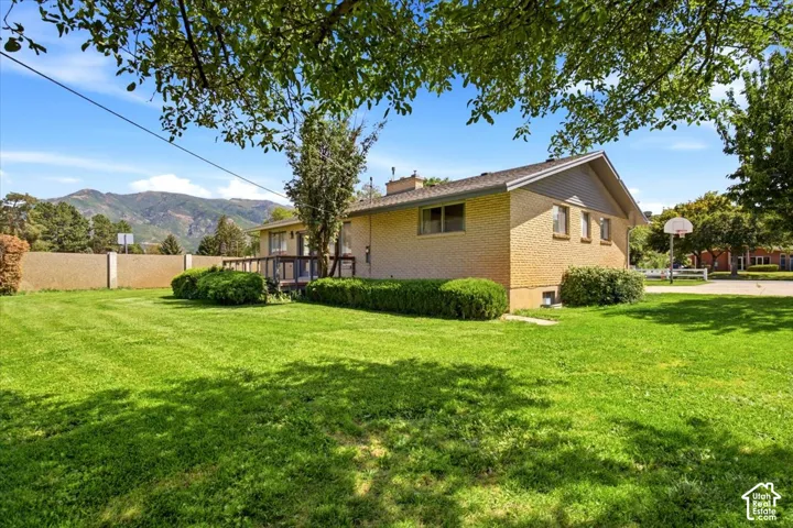 Expansive grassy yard with mountain backdrop, featuring a brick exterior and a raised deck