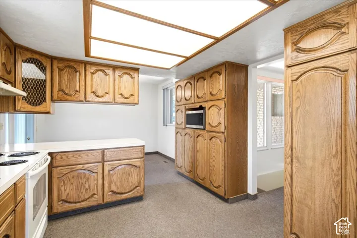 Extensive wood cabinetry, built-in microwave, white electric range, light-colored countertops, and overhead lighting panels