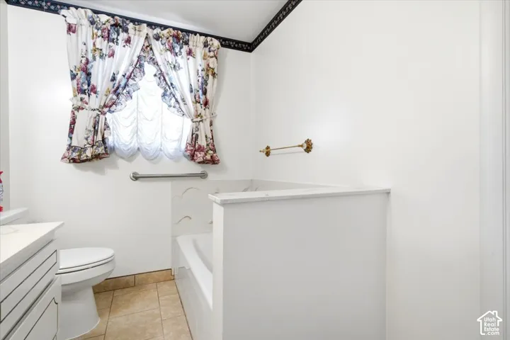 White bathroom featuring a built-in tub, white toilet, and neutral tile flooring