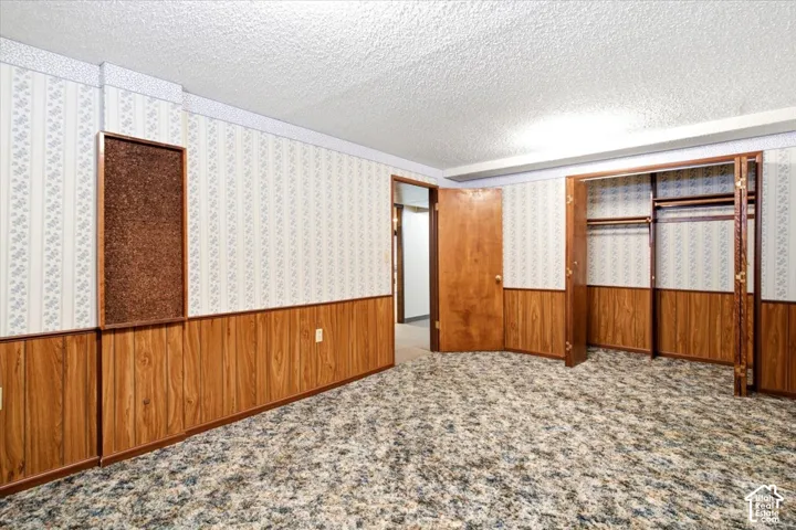 Patterned wallpaper, wood-finish wall paneling, textured ceiling, brown wood-finish doors, and built-in closet storage
