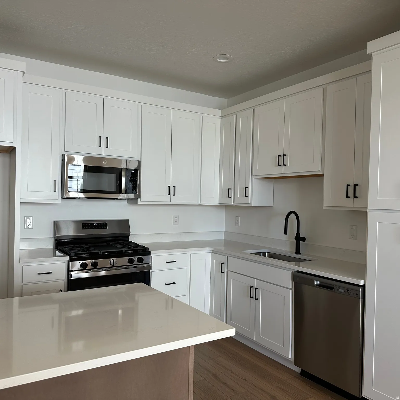 White shaker cabinetry, light-toned countertops, stainless steel appliances, and wood-finish flooring